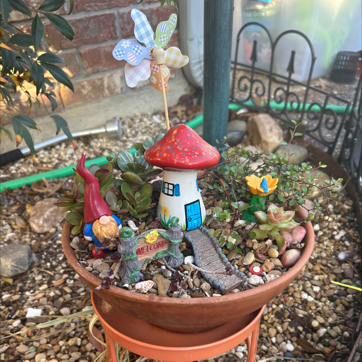 A pot with assorted succulents and decorative elements like a gnome and mushroom house.