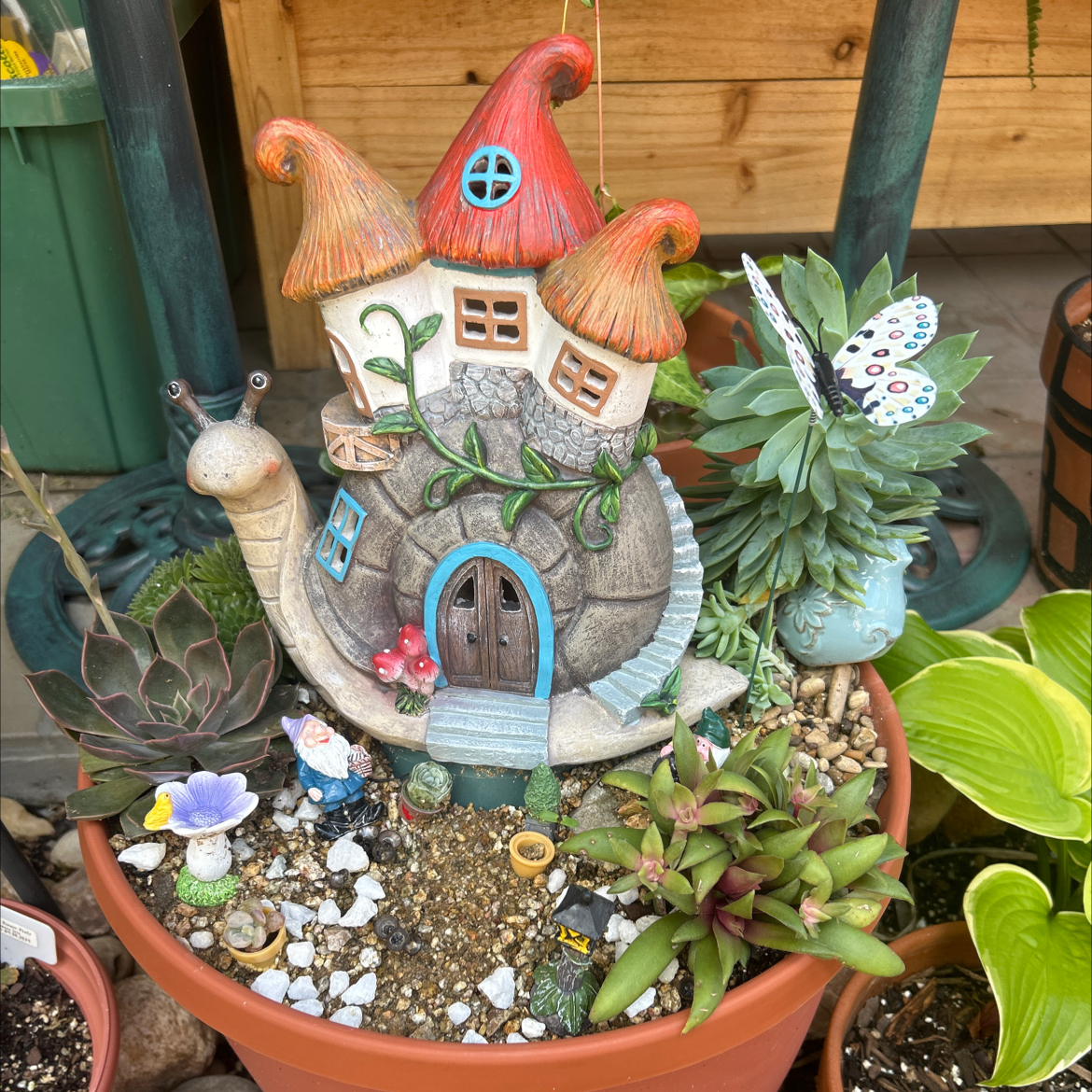 Assorted succulents in a pot with decorative elements including a snail-shaped house and small figurines.