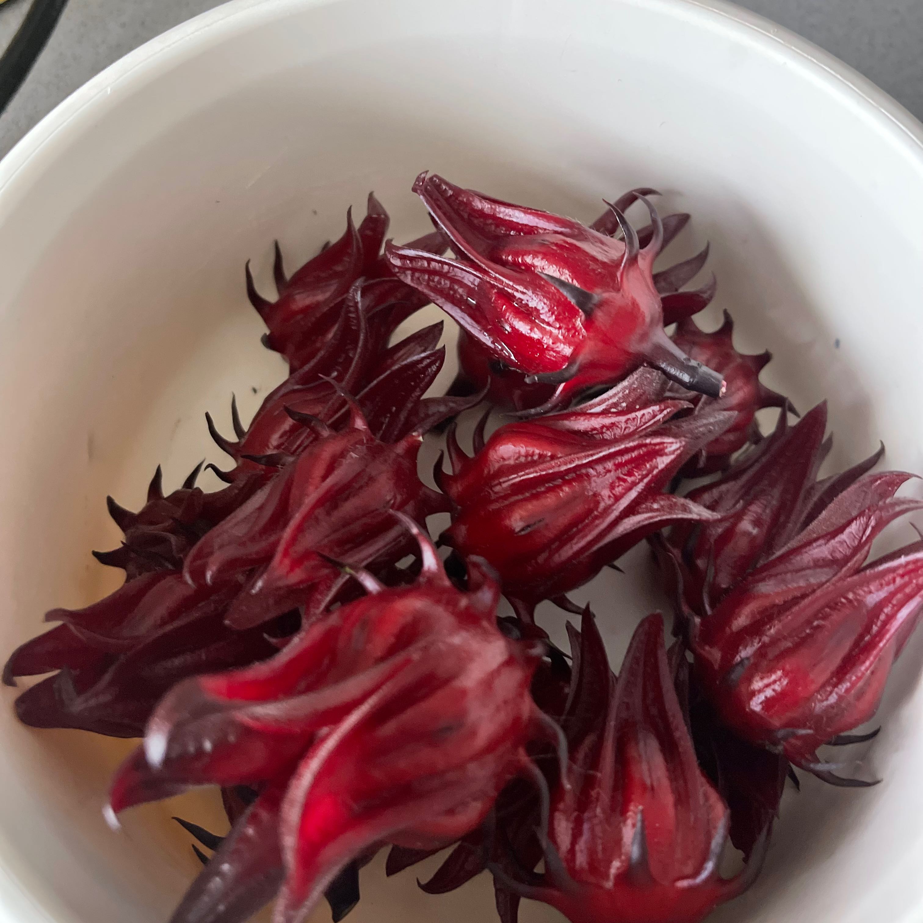Several red calyxes of the Roselle plant in a white bowl.