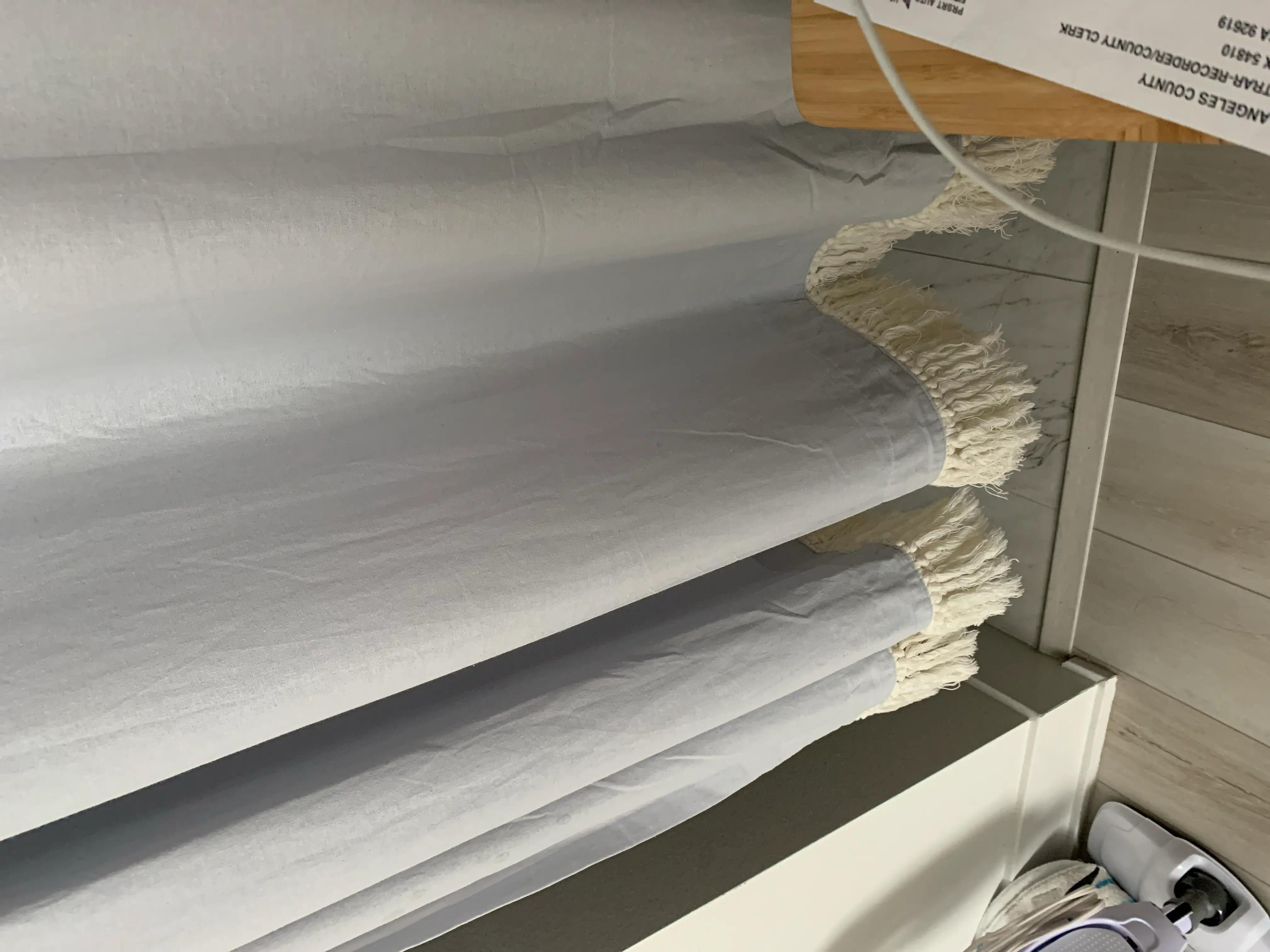 Image of a curtain or fabric with cords and a wooden surface, no plant visible.