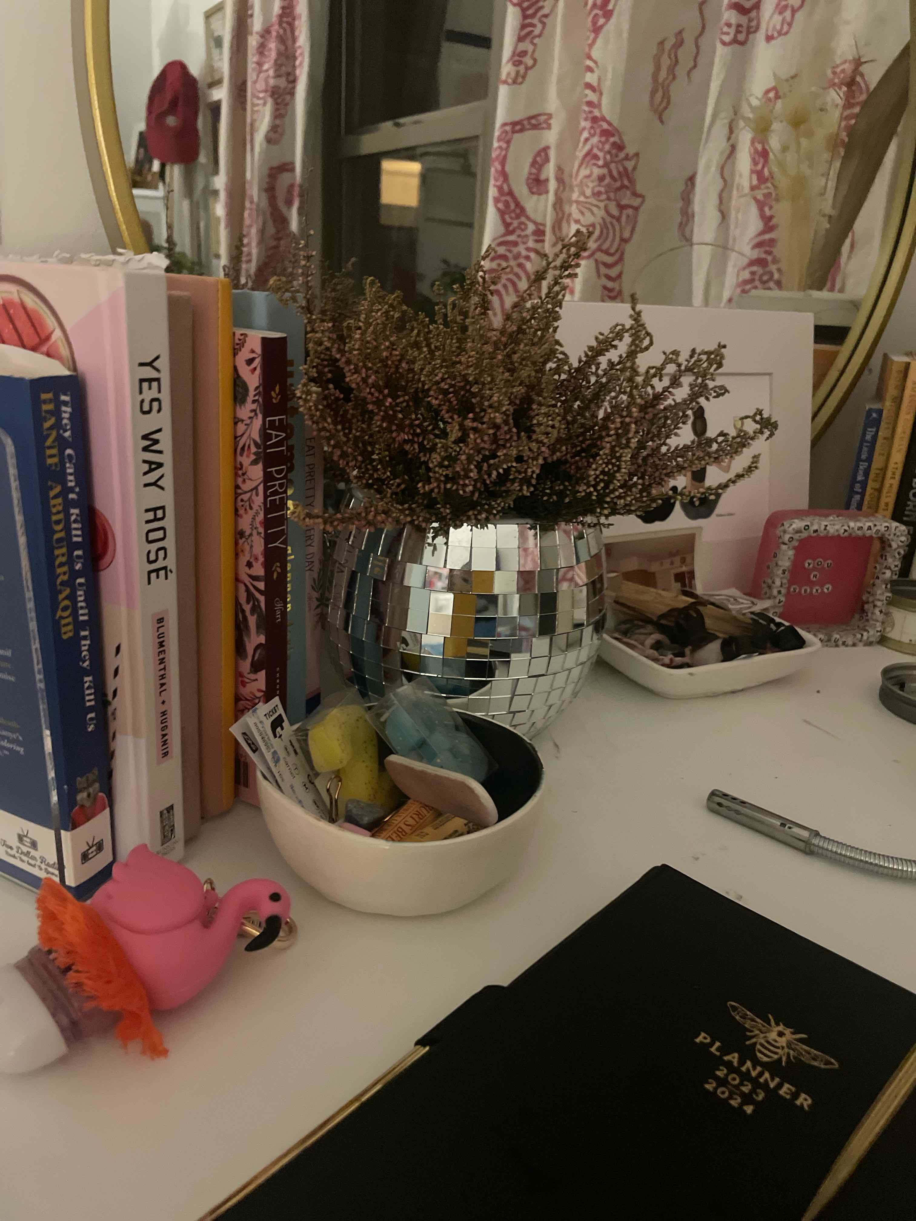 Heather plant in a reflective pot on a desk with books and small items.