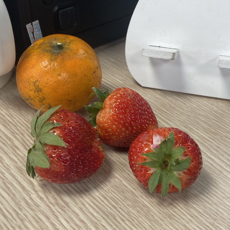 Three fresh strawberries and an orange on a wooden surface.