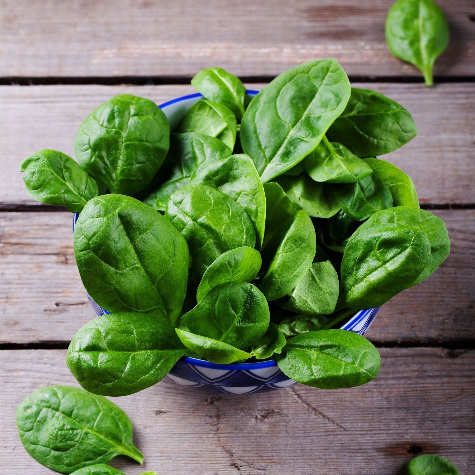 A bowl of fresh spinach leaves on a wooden surface.