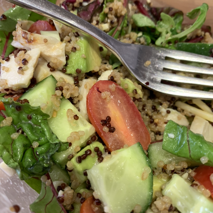 A close-up of someone's hands holding a healthy grain bowl or salad with quinoa, cucumber, tomato and other vegetables.