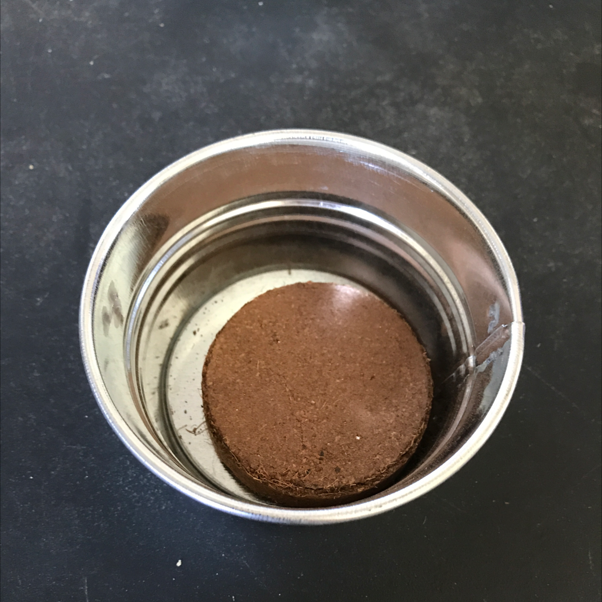 Close-up view of dry, brown potting soil or seed starting mix in a small metal cup or container