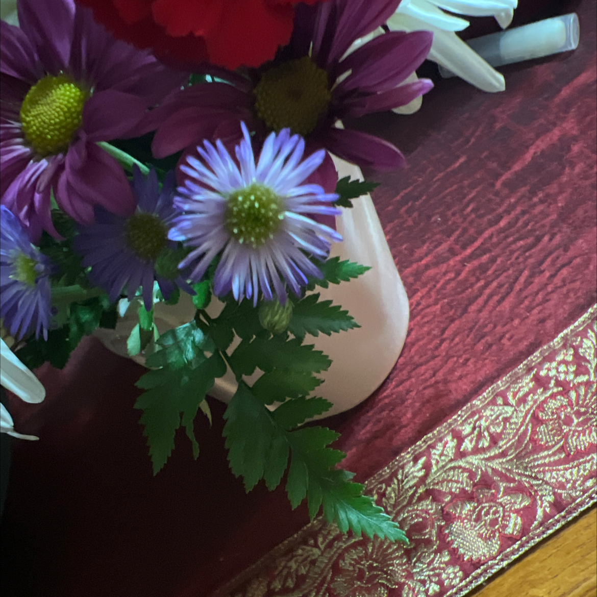 A bouquet of daisies and other flowers in a vase on a table.